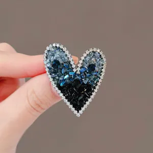 Close-up of heart-shaped brooch with blue and black crystals and rhinestone border.