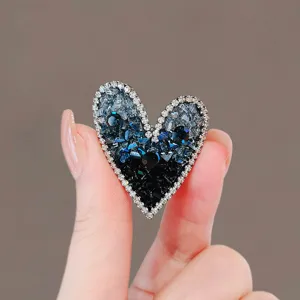 Detailed view of a luxury asymmetrical heart brooch with blue and black faceted crystals