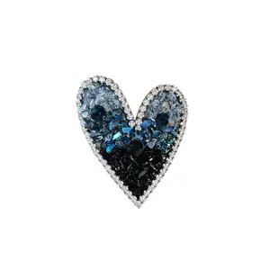 Detailed macro view of a heart-shaped brooch decorated with blue and black crystals.