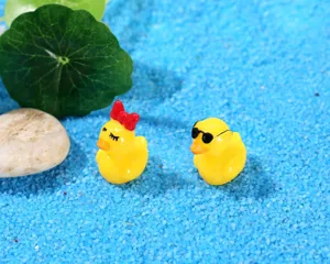 Close-up view of miniature couple resin ducks with bow and sunglasses in blue sand