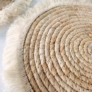 Close-up detail of a round straw woven placemat with elegant fringe edge, natural table decor.