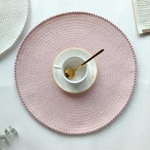 Round pink cotton woven placemat with delicate pom-pom border, ideal kitchen table mat detail.