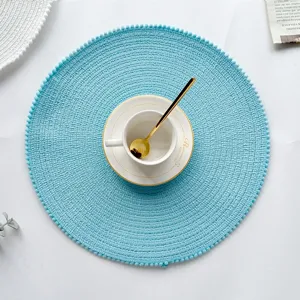 Detail shot of blue woven placemat with cute pom-pom edge, styled with chic teacup on white surface.