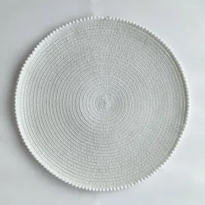 Detailed view of white round woven placemat featuring delicate pom-pom trim and texture.