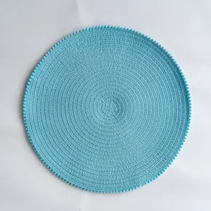 Detailed view of a round light blue braided placemat featuring a delicate pom-pom trim.