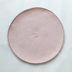Detailed view of a round woven placemat in pink with cute pom-pom edge. Perfect kitchen decor.