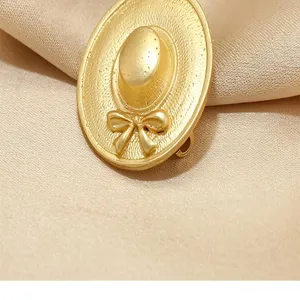 Detailed close-up of a vintage gold-toned hat shaped brooch with a bow, satin backdrop.