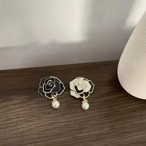 Detailed closeup of elegant camellia flower brooches with pearl pendants in black and white.