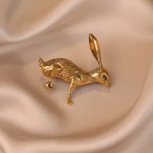 Gros plan d'une broche lapin dorée en métal vintage, montrant une texture et des détails sculptés.