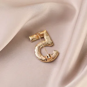 Close-up detail shot of a gold-toned number 5 brooch on silky fabric background.