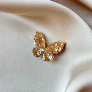 Detail view of a gold alloy butterfly brooch back showing secure pin lock on satin fabric.
