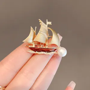 Close-up detail shot of the elegant gold sailboat brooch, featuring sparkling zircons and pearl.