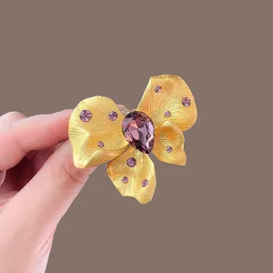 Elegant gold bow brooch featuring a sparkling purple rhinestone for women accessories.