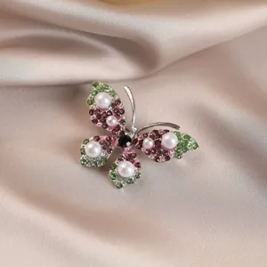 Detailed view of an elegant butterfly brooch with pink and green rhinestones and pearls