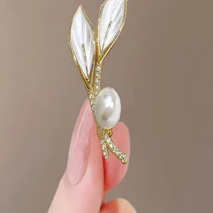 Macro detail of an elegant gold leaf brooch featuring a large pearl and tiny crystals