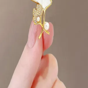 Close-up view of elegant golden ginkgo leaf brooch with white pearls and crystals