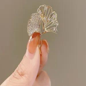 Detailed macro view of an elegant gold ginkgo leaf brooch with sparkling zircon inlay