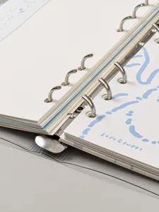 Gros plan des anneaux métalliques et des pages crème d'un carnet à anneaux A5.