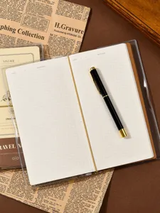 Close-up view of the grid notebook page with a sleek metal pen on retro newspaper detail.