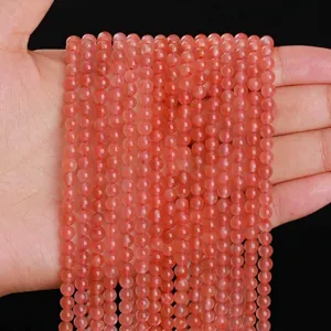 Fils de perles rondes naturelles en agate rouge du sud cerise tenus dans une main