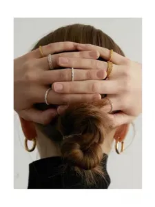 Detailansicht eleganter, minimalistisch vergoldeter Kettenringe an den Fingern eines Modells