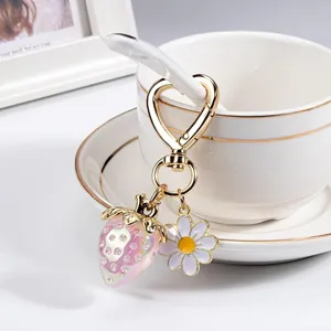 Detail of sweet strawberry and daisy charms on a gold heart-shaped keychain hook.