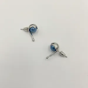 Detalle de pendientes de botón plateados con perlas azules y diseño de metal líquido