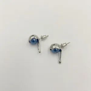 Vista macro de pendientes de metal plateado con diseño de goteo y perlas azules.