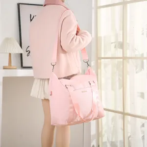 Large capacity pink travel bag with shoulder strap worn by model in a bright room