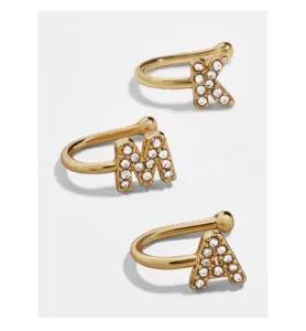 Κοντινό πλάνο τριών κομψών χρυσών ear cuffs σε σχήμα U με γράμματα από κρύσταλλα