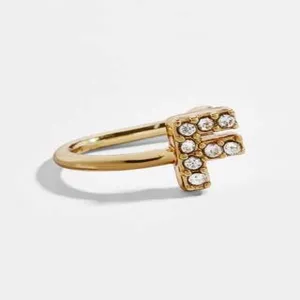 Λεπτομέρεια χρυσού σκουλαρικιού ear cuff σχήματος U με λαμπερό γράμμα F από στρας