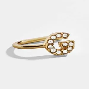 Κοντινή λήψη χρυσού ear cuff σε σχήμα U με το γράμμα G διακοσμημένο με αστραφτερά στρας.