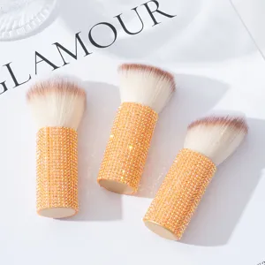 Dettaglio di tre pennelli da trucco professionali ricoperti di strass arancioni.