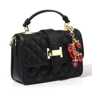 Close-up detail of sweet translucent strawberry charm on a luxury black quilted handbag