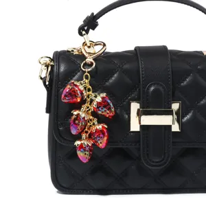Close-up detail of a translucent red strawberry bag charm on a black quilted handbag