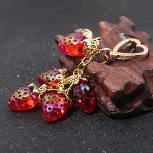 Detailed view of translucent red strawberry charms on a gold heart keychain.