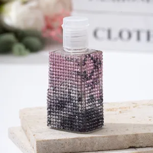 Close-up of a pink gradient rhinestone-covered travel spray bottle on a stone base