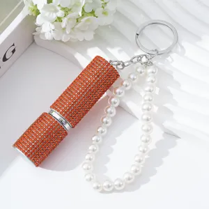 Detail of a 5ml orange rhinestone perfume atomizer keychain with elegant white pearls.