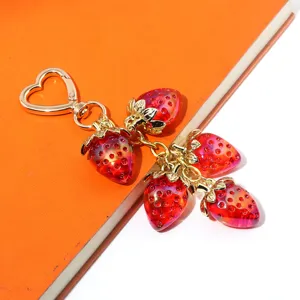 Close-up of translucent red strawberry charms on a gold-tone heart-shaped metal keychain
