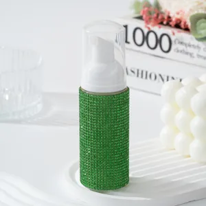 Gros plan d'une bouteille à pompe mousse en strass verts sur plateau décoratif blanc.
