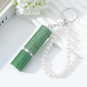 Macro detail of luxury green rhinestone perfume atomizer with white pearl keychain.