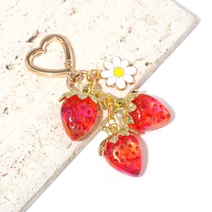 Close-up of translucent red strawberry charms and daisy flower on a heart keychain