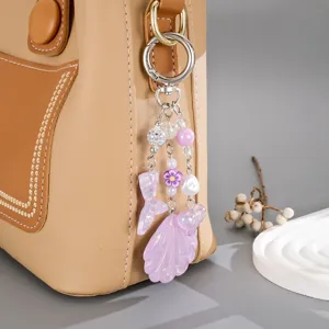 Détail d'une breloque sirène et coquillage en acrylique violet sur un sac en cuir marron.