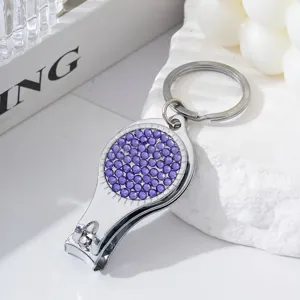 Detail of silver nail clipper keychain with purple rhinestones on white stone