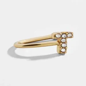 Λεπτομέρεια ενός χρυσού ear cuff σε σχήμα U με ένα διαμαντένιο γράμμα Τ σε λευκό φόντο.