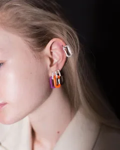Detailed close-up showing colorful enamel safety pin earrings and rhinestone ear cuff