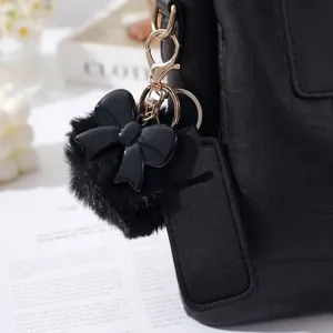 Close-up of elegant black faux fur pom-pom and bow keychain set with lipstick sleeve