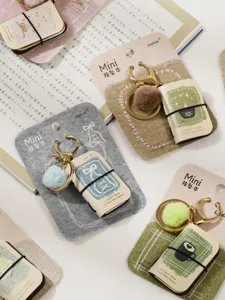 Mini notebook keychain detail view, cute PU leather book pendant with fluffy pom-pom.