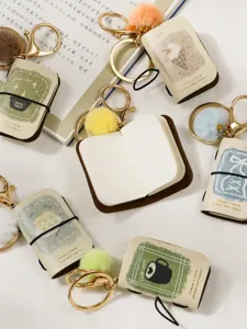 Detailed view of mini PU leather notebook keychains featuring cute plush balls and elastic bands.