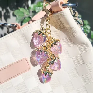 Close-up of translucent pink resin strawberry keychain charms on a gold chain hanging on bag
